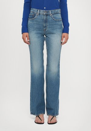 Ljusblå denimjeans med hög midja, rak passform och bleka detaljer. Bärs med en långärmad blå topp och flip-flops.