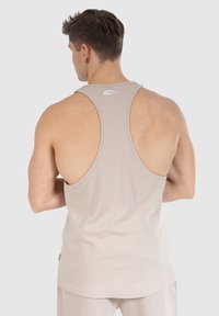 Beige mouwloze tanktop met een racerback ontwerp, gemaakt van zachte katoen, met een klein wit logo op de achterkant.