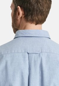 Lichtblauw button-up shirt met een standaard kraag, rugplooien en een gladde stofstructuur. Zichtbare stiksels bij de kraag en schouders.