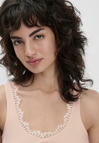 Lichtroze tanktop met een golvende kantafwerking langs de halslijn. Het materiaal lijkt glad en zacht, met een klassiek mouwloos ontwerp.