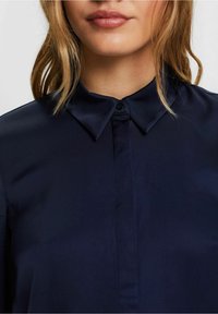 Mörkblå satin skjorta med klassisk krage, knäppning fram och en mjuk yta. Designen är enkel utan synliga mönster eller accentfärger.