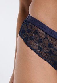 Biancheria intima in pizzo blu navy con motivo floreale e pois, con una fascia liscia in vita con il marchio "Etnam", che mostra cuciture dettagliate.