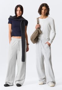 Zwei Modelle tragen lässige Outfits: ein navyfarbenscropped T-Shirt mit grauen Sweatpants und ein weißes Langarm-Henley mit grauen Sweatpants.