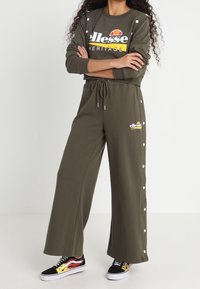 Olivgrön loungedräkt bestående av en sweatshirt med rund hals och logotyp, samt matchande vida byxor med tryckknappar på sidan.