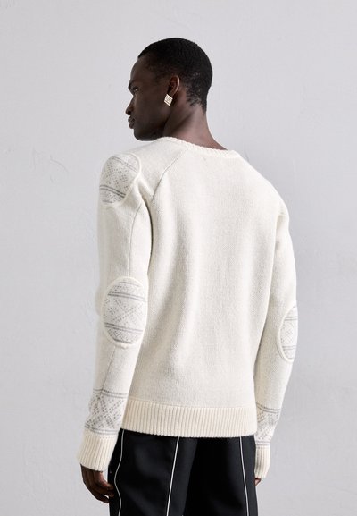 Weißer Strickpullover mit gemusterten Ellbogenpatches, gerippten Bündchen und rundem Halsausschnitt. Weiche Textur und lockere Passform mit minimaler Gestaltung.
