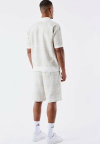 Chemise à manches courtes texturée beige clair et shorts assortis avec un motif subtil, complétée par des baskets blanches et des chaussettes.