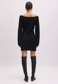 Schwarzes geripptes Strickkleid mit schulterfreiem Ausschnitt, langen Ärmeln und taillierter Silhouette, kombiniert mit kniehohen schwarzen Lederstiefeln.