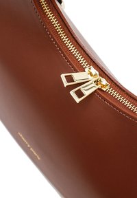 Sac à main en cuir marron avec une fermeture éclair dorée dotée de deux tirettes décoratives, texture lisse et logo embossé à l'avant.