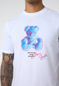 White cotton t-shirt featuring a blue bear graphic with red accents, displaying text related to "Closure" and cities: London, Milan, Tokyo.