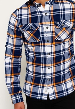 Chemise à manches longues bleu, blanc et orange à carreaux avec un col boutonné, deux poches poitrine et des boutons noirs. Texture flanelle douce.