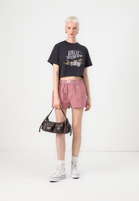 Black cropped t-shirt with graphic print, red and white checked shorts, black handbag, and white high-top sneakers. Smooth textures throughout.