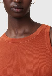 Geribbelde oranje tanktop met brede halslijn en armsgaten, vervaardigd uit een zachte stof met zichtbare stikdetails.