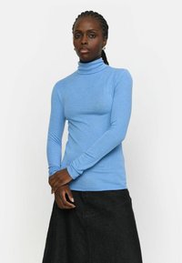 Blaues Langarm-Turtleneck-Oberteil aus glattem Stoff, kombiniert mit einem schwarzen Rock. Das Turtleneck hat ein figurbetontes Design und ist dehnbar.