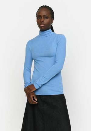 Mėlynos ilgos rankovės turtleneck tipo palaidinė, pagaminta iš lygaus audinio, derinama su juoda sijonu. Turtleneck yra prigludusio dizaino ir elastingos medžiagos.