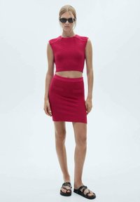 Fitted two-piece set in vibrant magenta. The sleeveless crop top features ribbed texture, while the knee-length skirt has front pockets.