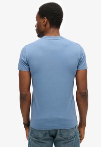 Camiseta azul de manga corta hecha de algodón, con cuello redondo y una textura suave, combinada con jeans de mezclilla azul desgastados.