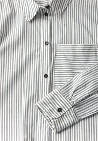 Camicia a righe con bottoni bianchi e grigi. Presenta un colletto, bottoni neri e una tasca con righe orizzontali. Texture liscia.