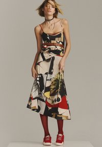 Maxi dress with a multicolored abstract pattern, featuring thin straps, a belted waist, and a soft drape. Paired with red sneakers.