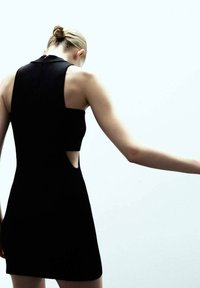 Czarna suknia bez rękawów z wysokim dekoltem i wycięciem po bocznej stronie, wykonana z gładkiego, dopasowanego materiału.