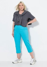 Haut gris à manches courtes avec un pull drapé autour du cou, associé à un pantalon court bleu vif et des baskets blanches.