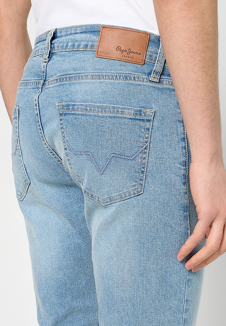 Pantalones vaqueros de mezclilla azul claro con un ajuste slim, bolsillos traseros con costura en forma de V y un parche de cuero marrón con la marca en la cinturilla.