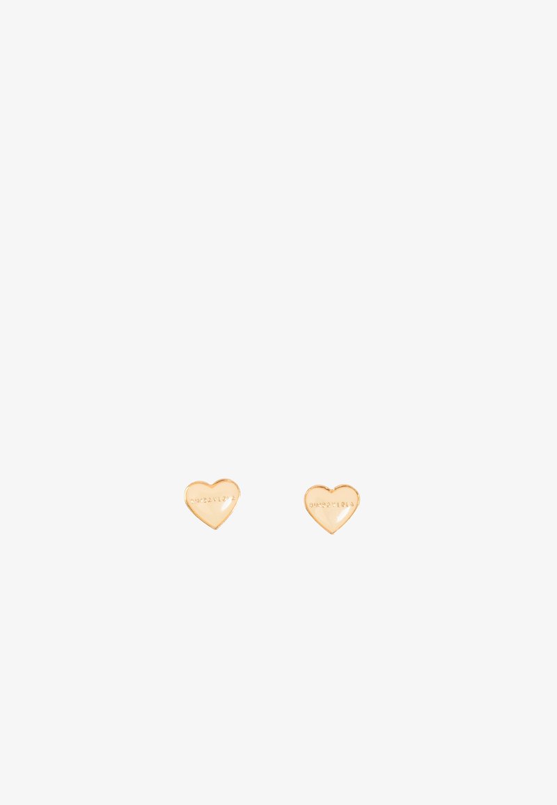 Un par de pequeños pendientes de oro en forma de corazón con un sutil texto grabado sobre un fondo blanco.
