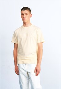 Lichtgele katoenen t-shirt met een ronde halslijn en korte mouwen, voorzien van een reliëf "Timberland" logo op de voorkant. Draag het met witte broeken.