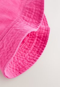 Chapeau seau rose en tissu doux, texture matelassée. Présente un large bord et des détails cousus autour du bord. Design simple et décontracté.