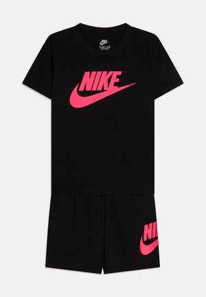 Črna bombažna majica s kratkimi rokavi z velikim rožnatim logotipom Nike. Ujemajoče se črne kratke hlače z rožnatim logotipom Nike na levi strani.