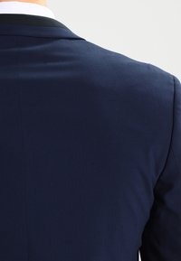 Marinblå blazer med en slät textur och strukturerad design, med en kontrasterande svart krage. Bakvy som framhäver den skräddarsydda passformen.