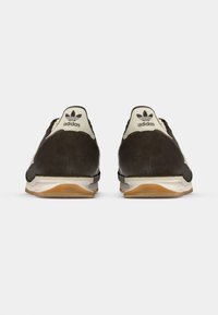 Czarne zamszowe sneakersy z białymi akcentami, z fakturowaną tylną częścią, charakterystycznym logo na pięcie oraz kontrastującą gumową podeszwą.