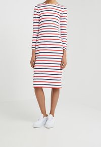 Raidallinen mekko, jossa on pitkät hihat valkoisena, laivastonsinisenä ja punaisena. Tiukka malli, polvimittainen, yhdistettynä valkoisiin tennareihin. Sileä kankaan pinta.