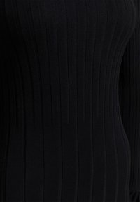 Černý žebrovaný pletený svetr se vertikálními pruhy, přiléhavým střihem a hladkou texturou. Žádné ozdoby ani akcenty nejsou viditelné.