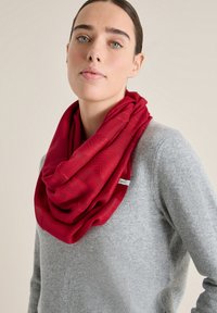 Rød infinity-scarf lavet af blødt stof med en glat overflade og subtilt mønster, båret over en lysegrå sweater.