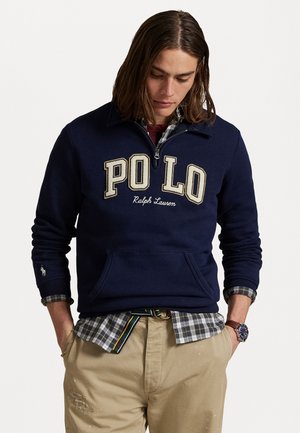 Marineblauwe sweatshirt met een half-rits ontwerp, opvallende "PO LO" borduring, een voorkhuis en geribde manchetten. Gekocht met een geruit shirt en beige broek.