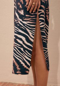 Magas hasítású ruha puha anyagból, sötét alappal és világos tigristcsíkos mintával. Karcsú sziluettet és hangsúlyozó oldalsó hasítékot kínál.