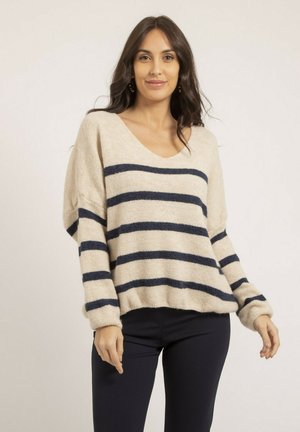 Pull beige avec des rayures horizontales navy, coupe ample, décolleté en V profond, manches longues et poignets côtelés. Texture douce, design décontracté.