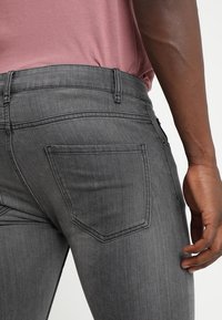 Grå denimjeans med en figurnära design, klassisk bakficka och en mjuk textur, kombinerat med en kortärmad rosa skjorta.