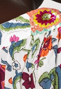 Multibarevný květinový top s detailem na rameni posetým flitry. Vyrobeno z lehkého materiálu s jemnou výšivkou v jasných barvách.