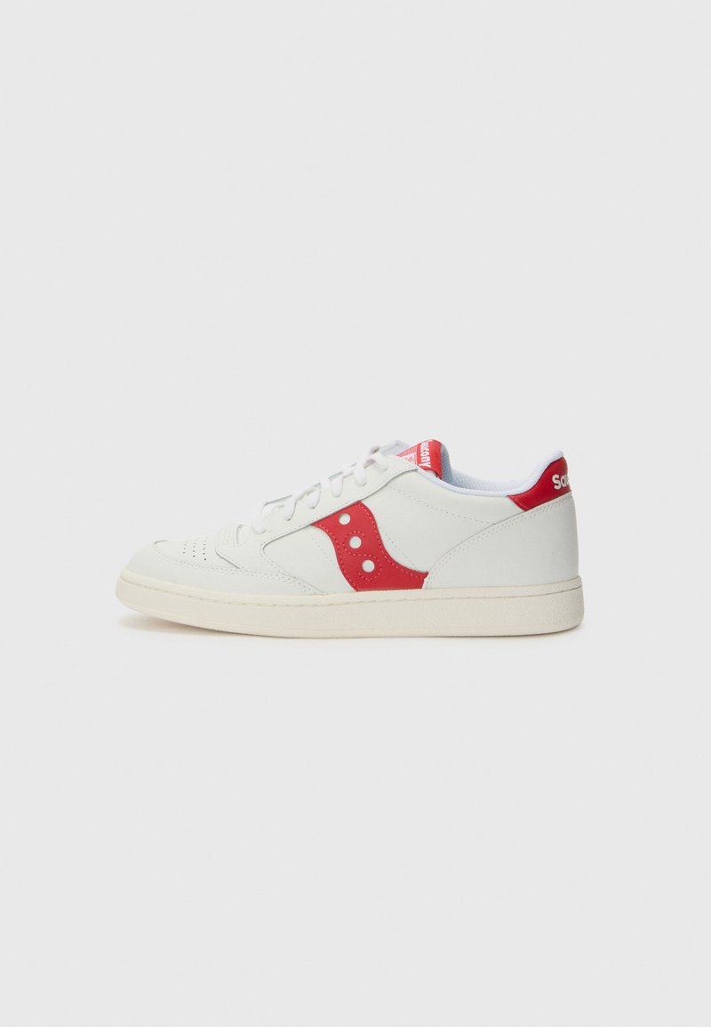 Zapatilla blanca con acentos rojos, con parte superior de cuero suave, detalles perforados en la punta y una suela de goma texturizada color crema.