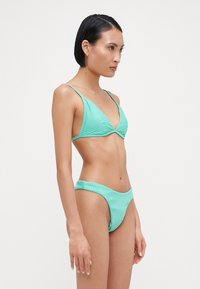 Myntgrön ribbad bikini med en triangulär bralette-topp och lågmidjade underdelar. Har tunna stölpor och en jämn textur utan synliga mönster.