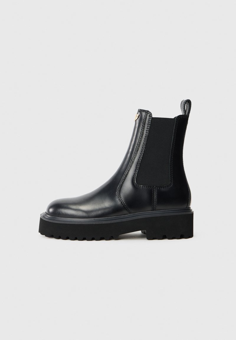 Czarne skórzane botki sięgające kostki z elastycznymi panelami bocznymi, okrągłym noskiem oraz masywną czarną gumową podeszwą z teksturowanym wzorem zapewniającym przyczepność.