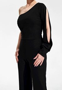 Schwarzes, ein Schulter Top mit taillierter Passform und langem Ärmel, der mit einem Cut-Out-Detail versehen ist. Hergestellt aus glattem Stoff; passt gut zu weiten Hosen.