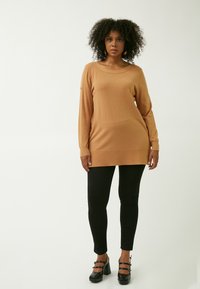 Brun langærmet sweater med bred halsudskæring, parret med sorte tætsiddende leggings og sorte hæle. Simpelt design og behagelig pasform.