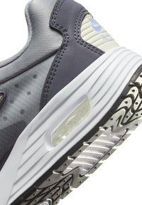 Szürke sneaker, hálós és bőrből készült anyagokkal. Jellemzője a fehér középtalp, átlátszó párnázó egység és a texturált gumitalp a tapadás érdekében.