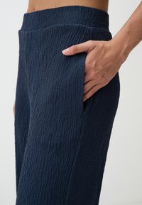 Marineblauwe gestructureerde broek met ribbelafwerking en zijzakken. De tailleband is elastisch voor comfort en een casual pasvorm.