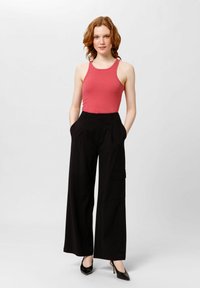 Pantalones anchos negros con bolsillos laterales, combinados con una camiseta de tirantes rosa ajustada. El conjunto se complementa con zapatos de tacón altos negros.