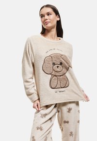 Cream-colored fleece top with dog design and "be sweet" text; paired with matching pants featuring a brown dog pattern. Soft texture, relaxed fit.