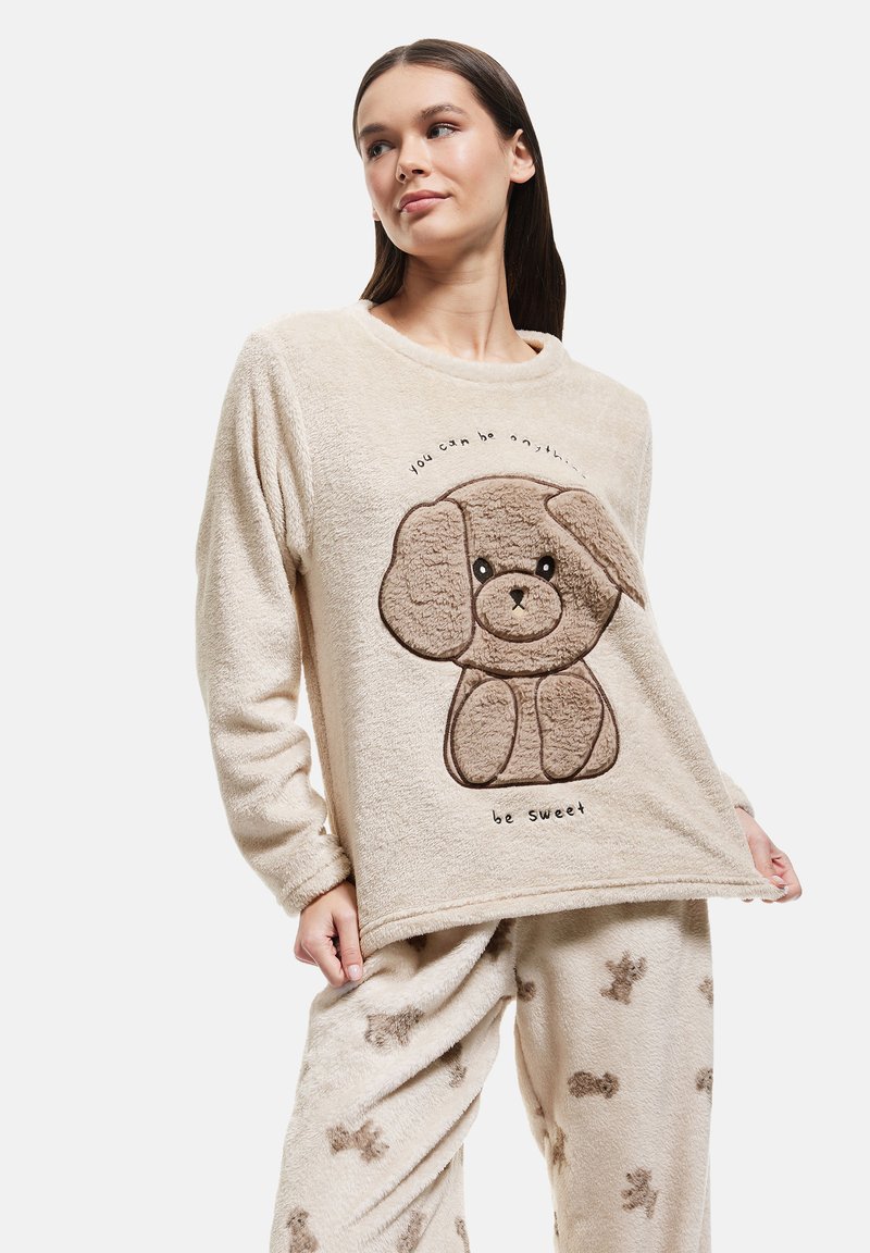Cream-colored fleece top with dog design and "be sweet" text; paired with matching pants featuring a brown dog pattern. Soft texture, relaxed fit.