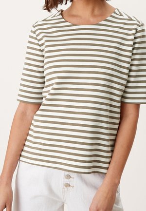 Vrouw draagt een beige-wit horizontaal gestreept topje met korte mouwen, gecombineerd met witte hoge taillebroeken met twee knopen.